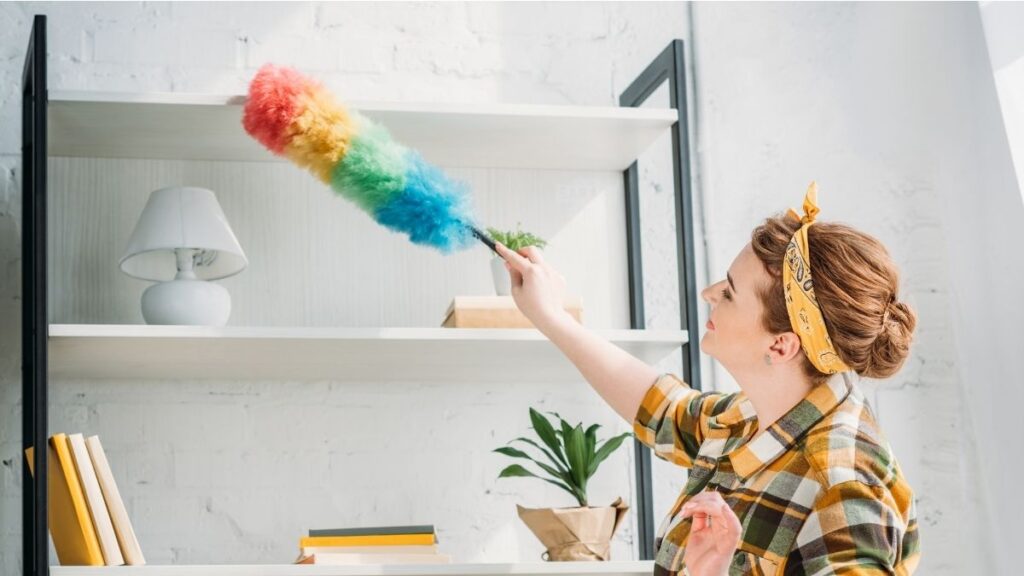 Woman dusting high shelves first as part of a top-to-bottom home cleaning routine